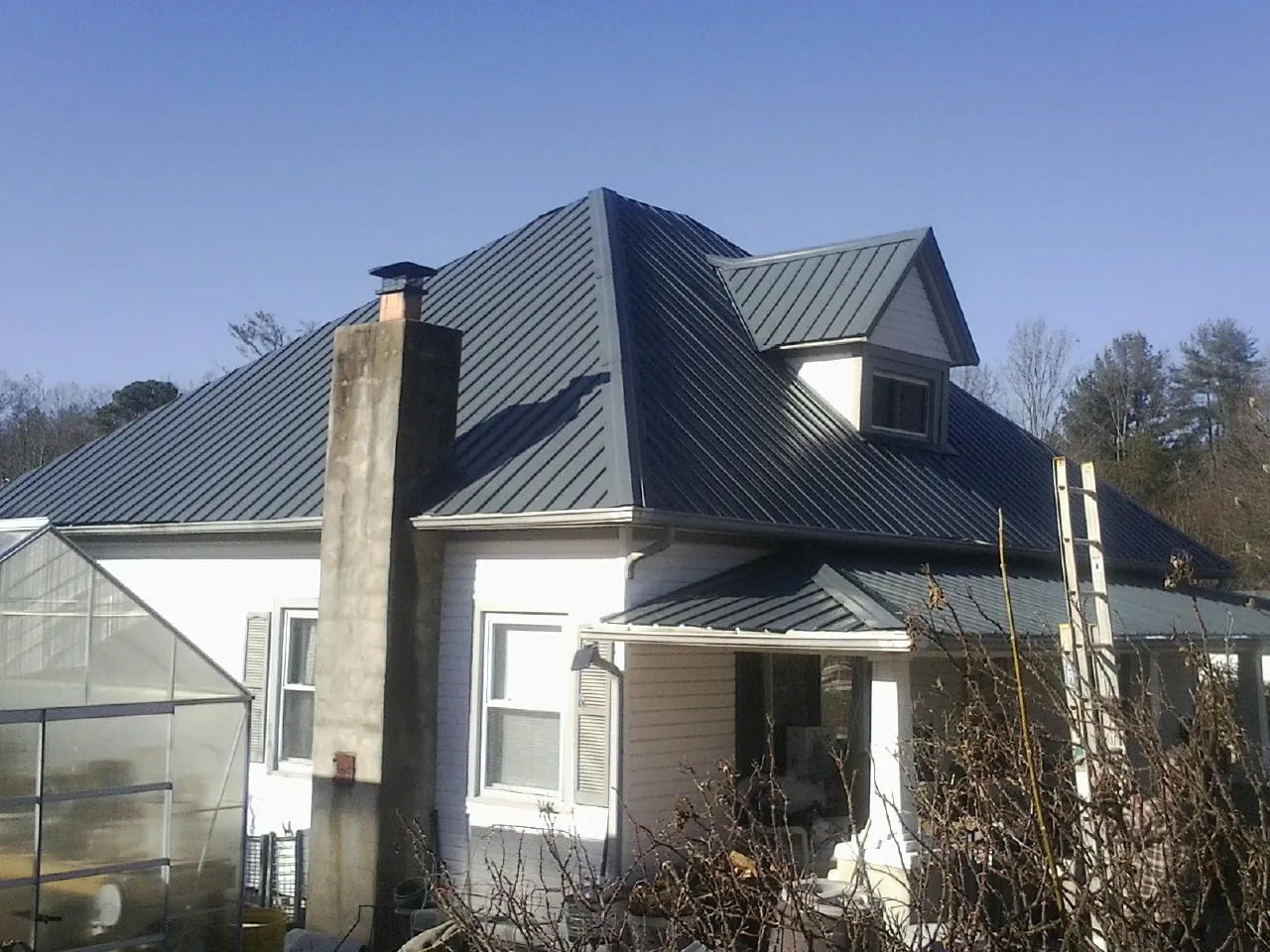 Dark blue standing seam metal roof on a white farmhouse with dormer — Slate & Tile Roof Repair by Roofing Brothers in Macedon