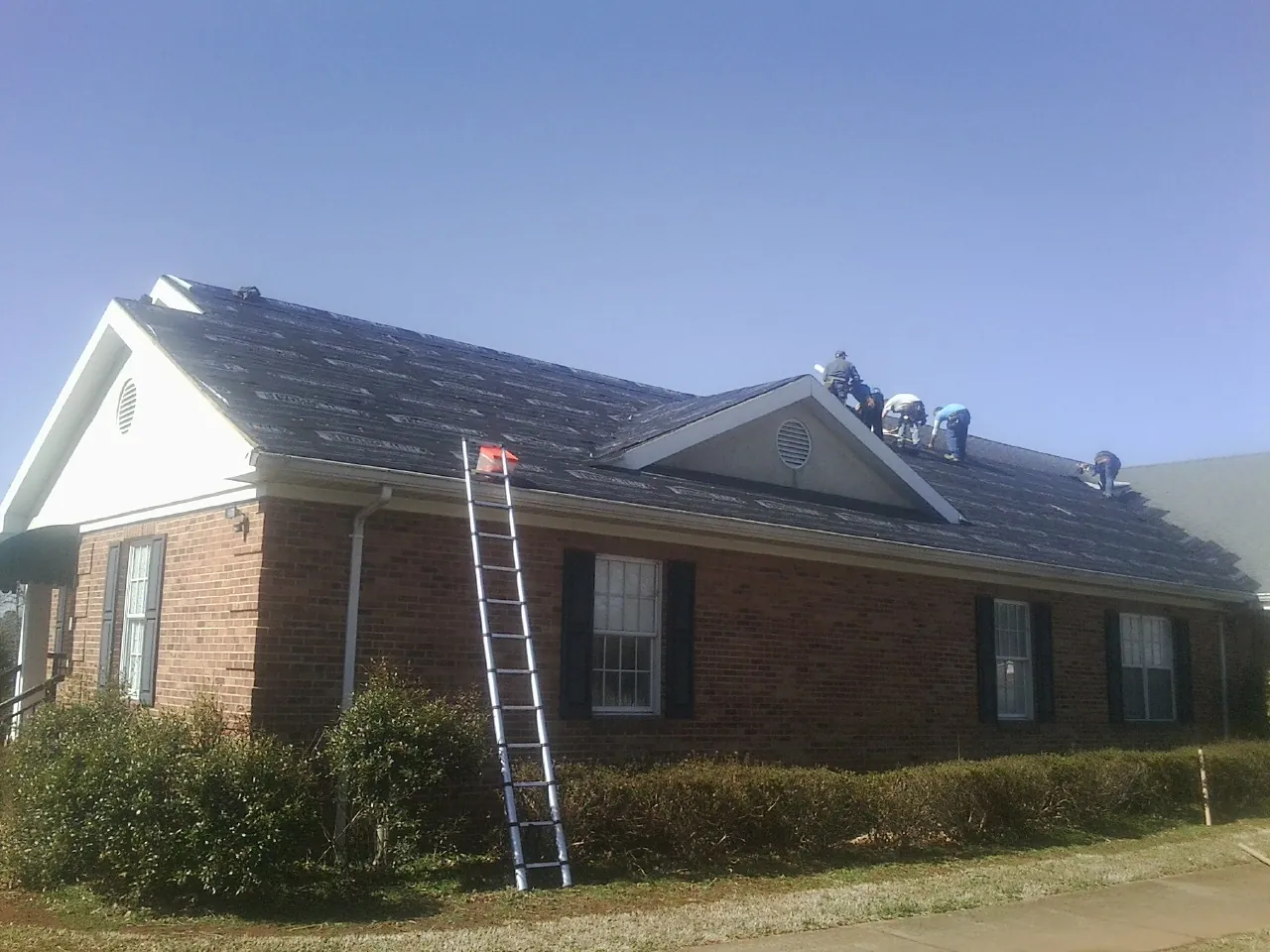Crew tearing shingles off a brick ranch roof with a ladder set — Metal Roof Repair work by our crew in Macedon