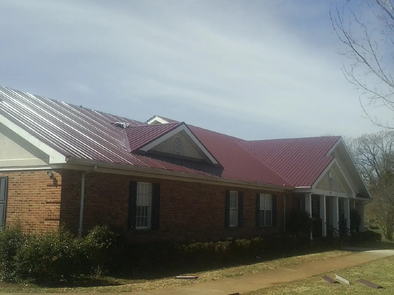 Red metal roof with gabled entries on a long brick building, from a Hail Damage Roof Repair job in Macedon