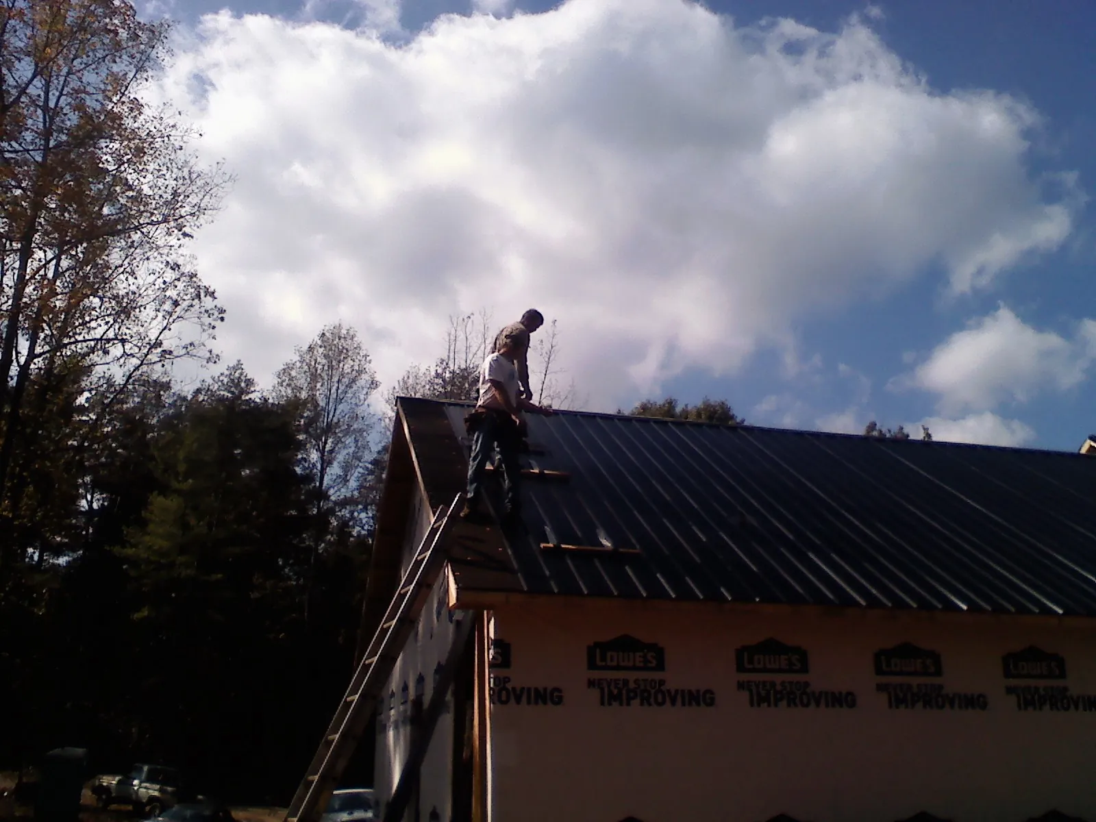 Roofer fastening dark metal panels high against a cloudy sky, from a Roof Inspection job in Macedon