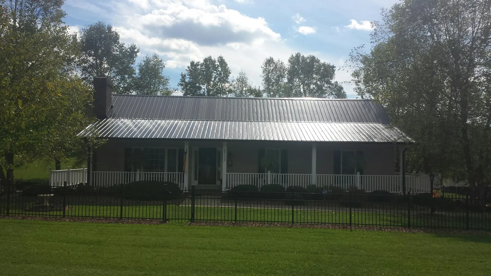 Gray metal roof on a brick ranch with a full width front porch — Gutter Guard Installation work by our crew in Macedon
