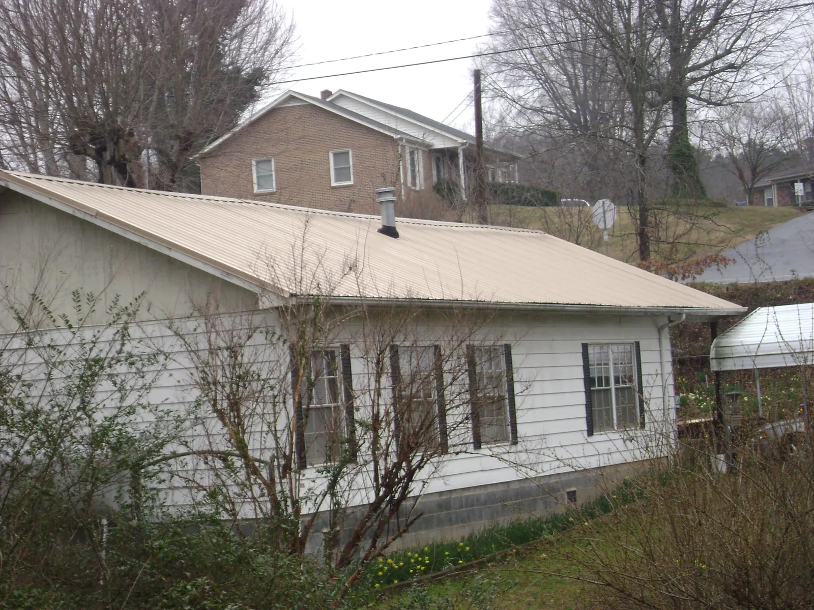 Tan metal roof on a white sided house set into a hillside — Commercial Roofing by Roofing Brothers in Macedon