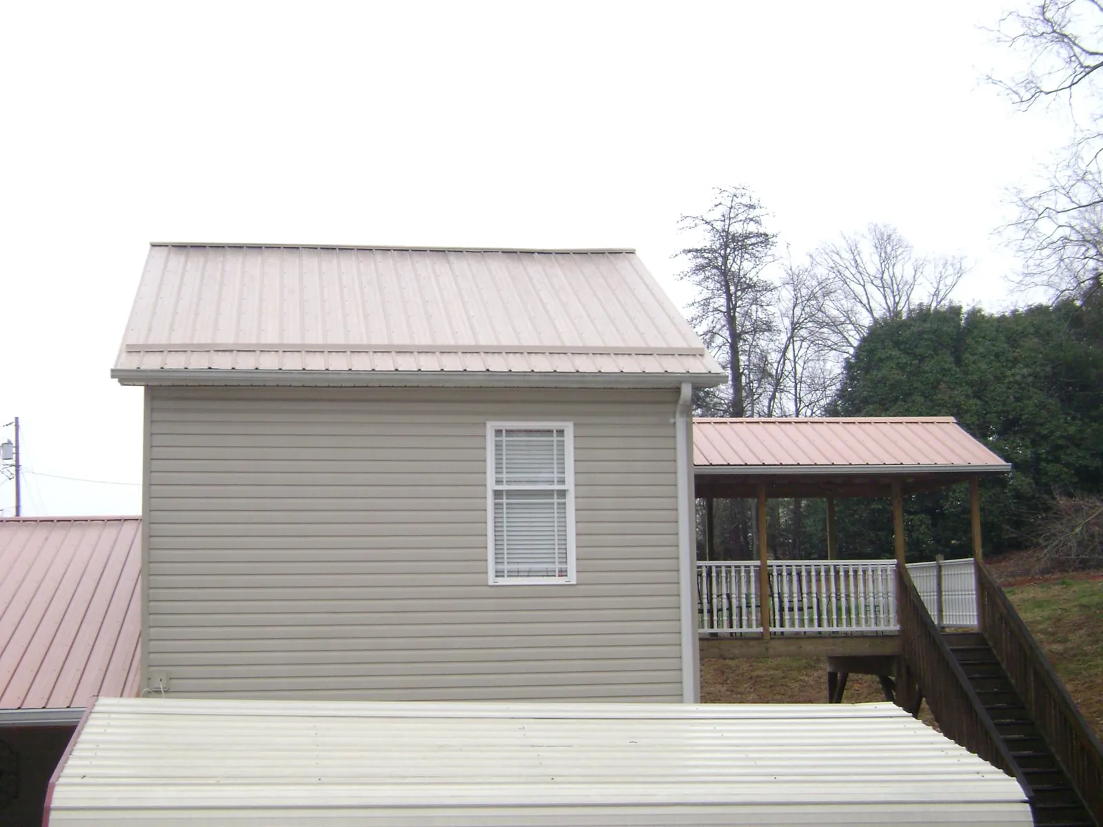 Tan metal roofs on a two story addition and attached porch, from a Roof Replacement job in Macedon